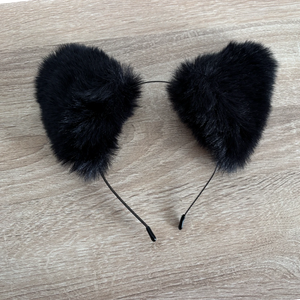 Black faux fur cat ears headband displayed on a light wood grain surface.
