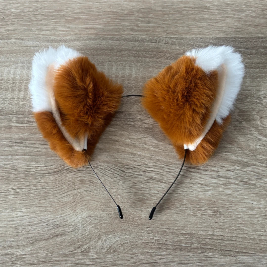 A pair of fluffy faux-fur animal ears, styled like a fox or rabbit, in brown and white, attached to thin black headbands, displayed on a light wood floor.