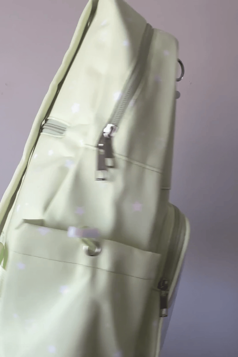 A pastel yellow-green Ita backpack with silver zippers and a white star pattern, shown in a close-up angled view against a plain light background.