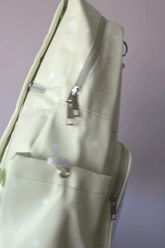 A pastel yellow-green Ita backpack with silver zippers and a white star pattern, shown in a close-up angled view against a plain light background.