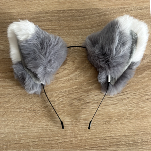 Gray and white faux fur cat ears headband on a light brown wooden surface.