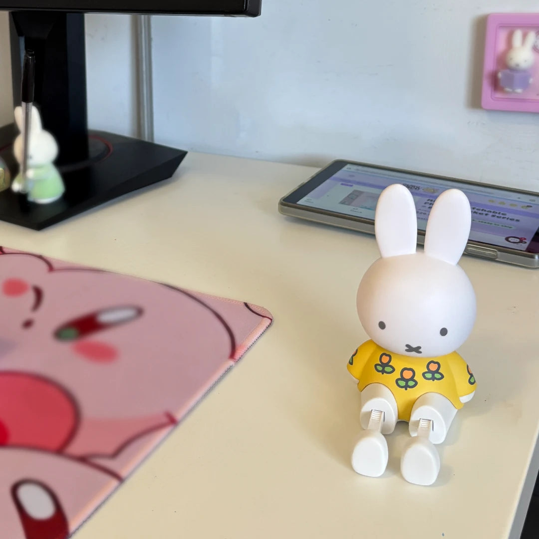 Small Bunny shaped phone holder in a yellow dress on a desk with a tablet and mouse pad in the background.