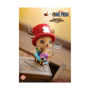 Cosplay Chopper from One Piece in a logged version, wearing a red hat with a white cross and a purple top, sitting on a book on a wooden deck. Features Hot Toys and Netflix One Piece branding.