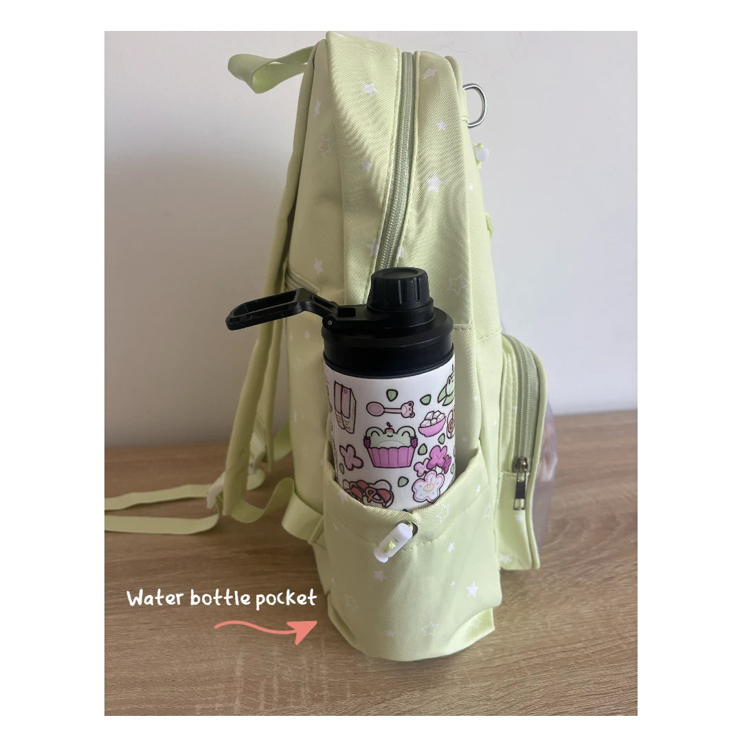 A pale yellow-green Ita backpack with a side water bottle pocket holding a white insulated bottle with a black lid and pink cartoon print. The photo is taken on a wooden surface against a plain wall, with the text 'Water bottle pocket' and an arrow pointing to the pocket.