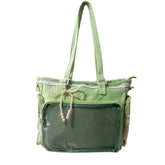 A green tote bag with a front mesh pocket, white lace trim, and a decorative pearl bow accessory hanging from the handle, shown against a plain white background.