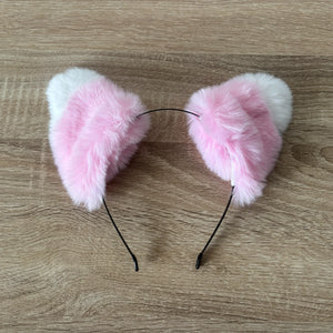 Pink and white faux fur cat ears headband on a light brown wood grain background.
