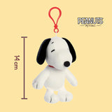 Plush keychain of Snoopy dog with a red tag on a yellow background, featuring the Peanuts logo.