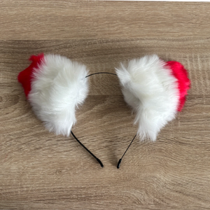 A fluffy faux-fur ears in white and red, resting on a light brown wood-grain surface.
