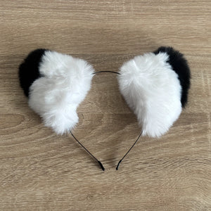 Black and white faux fur cat ears headband on a light brown wood grain background.