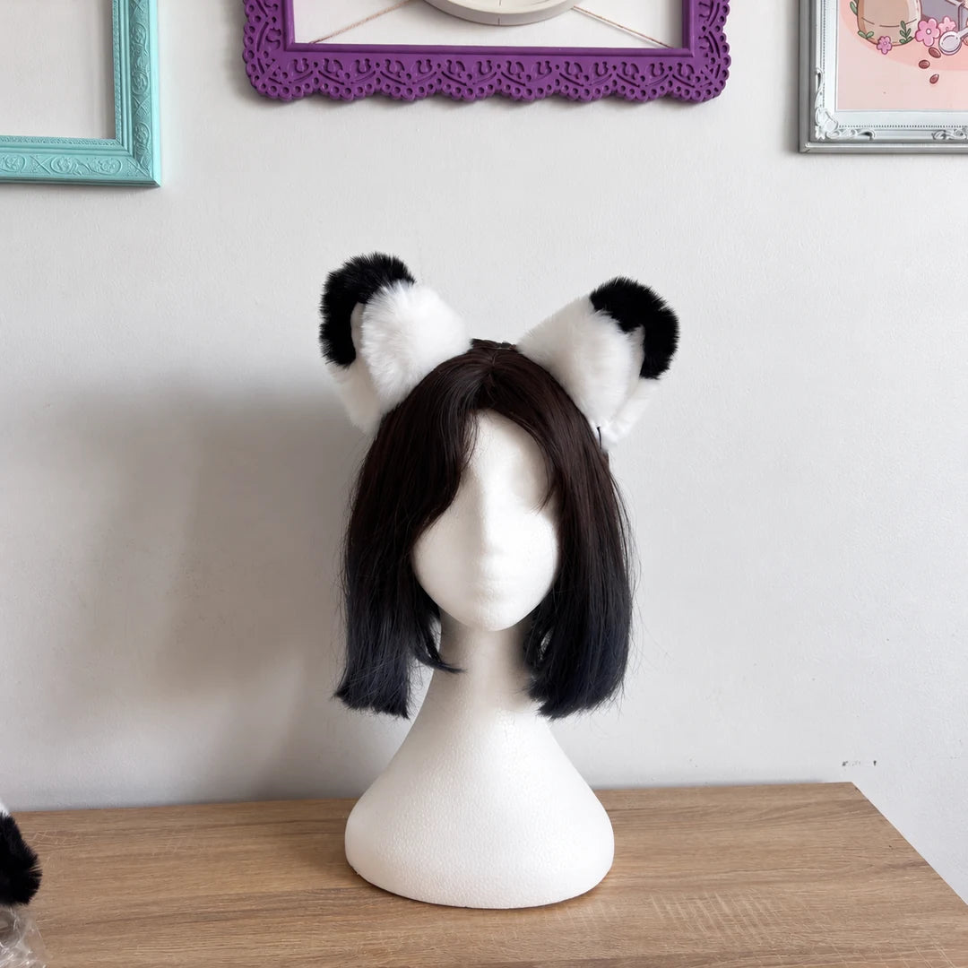 A short black wig with fluffy black-and-white cat ears is displayed on a white mannequin head, set on a wooden table against a light wall with framed pictures.