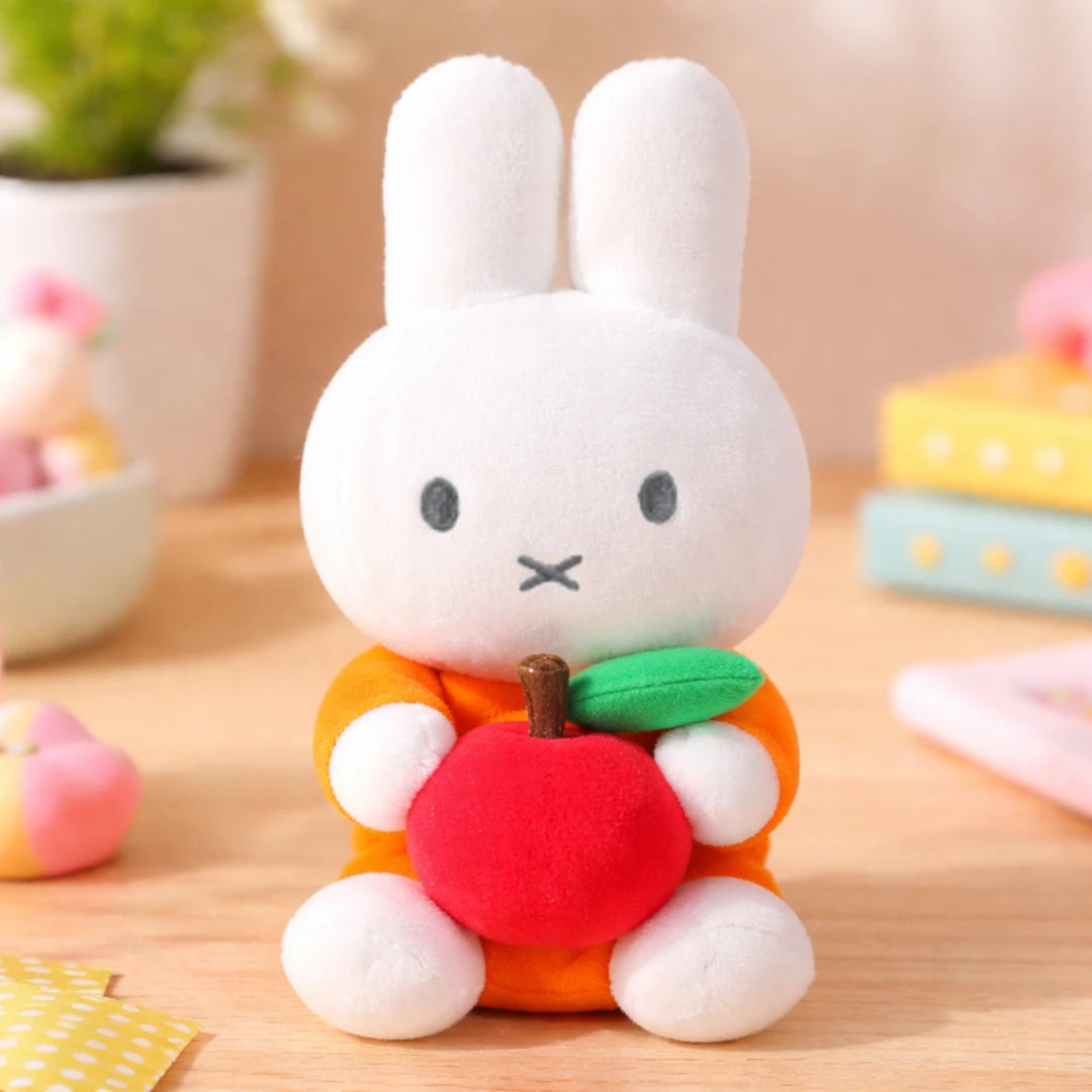 White Miffy the bunny plush toy with a red apple on a wooden surface