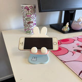 Miffy Phone stand with an iphone on a desk next to a colorful mug and monitor
