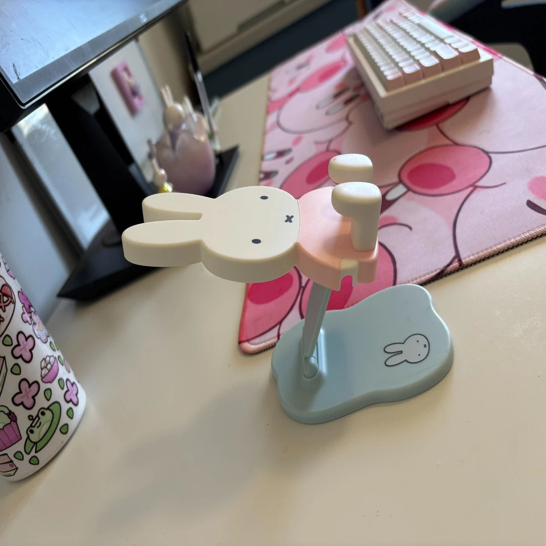 Desk setup with a cartoon-themed mouse pad and MIffy the Bunny shaped phone stand in pastel colours