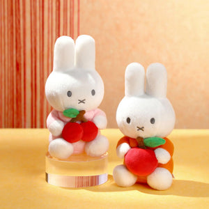 Two plush toys resembling bunnies with red apple and red cherries on a yellow surface.