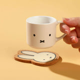 Hand holding a white Miffy mug with a coaster. Blind box