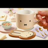 Hand holding a white Miffy mug with a coaster. Blind box