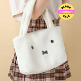 White plush bag with a face design held by a person wearing a plaid skirt