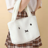White plush bag with a face design held by a person wearing a plaid skirt