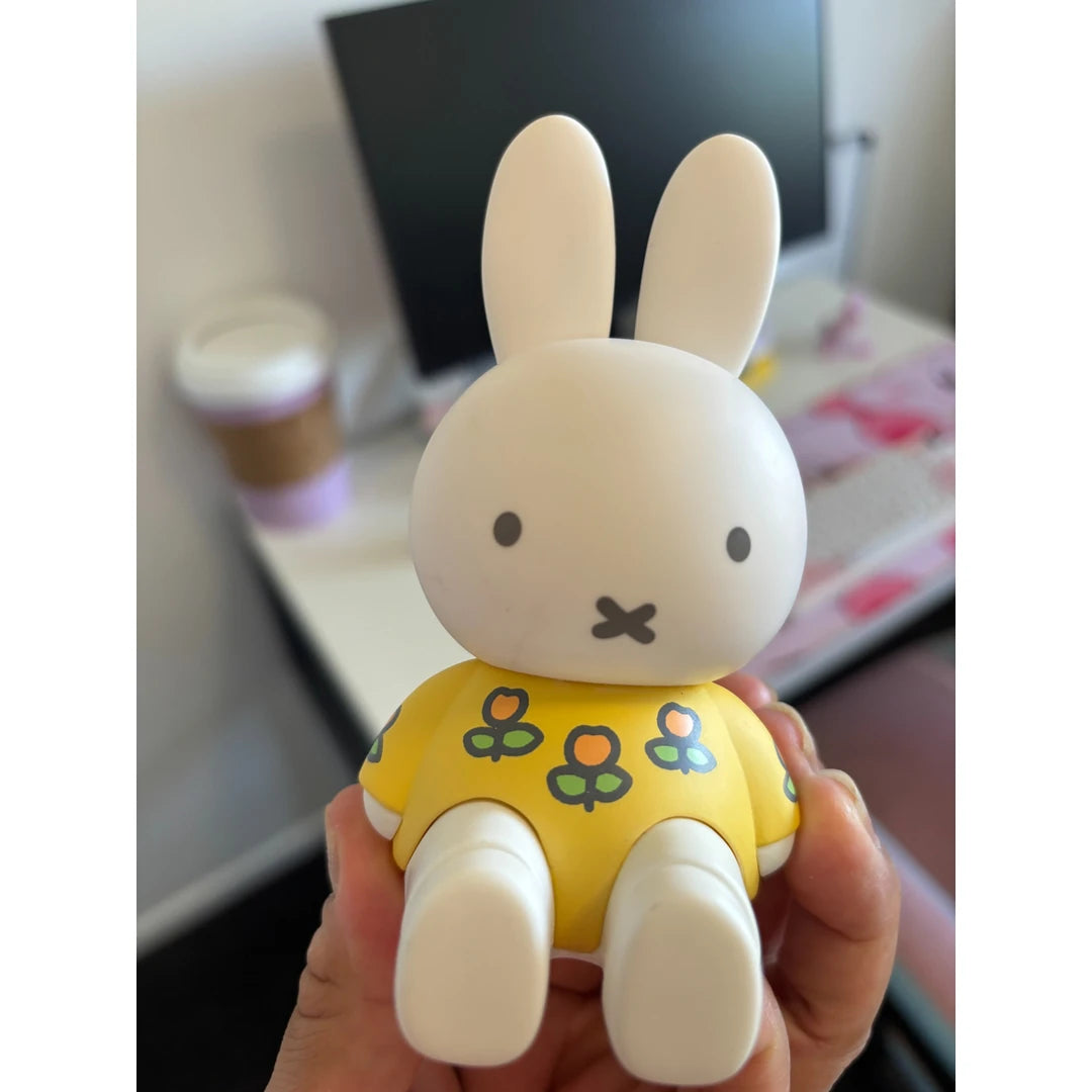 White rabbit Phone or pad holder with a yellow outfit featuring green leaves held in a hand. Miffy blind box item, phone stand