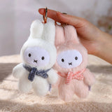 Two fluffy keychains, one white with a blue scarf and one pink with a bow, held by a hand. Surprise box