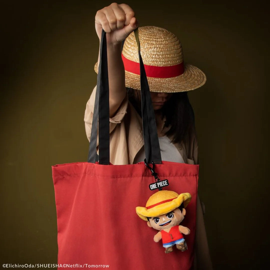 Person holding a red tote bag with a plush toy and straw hat against a brown background