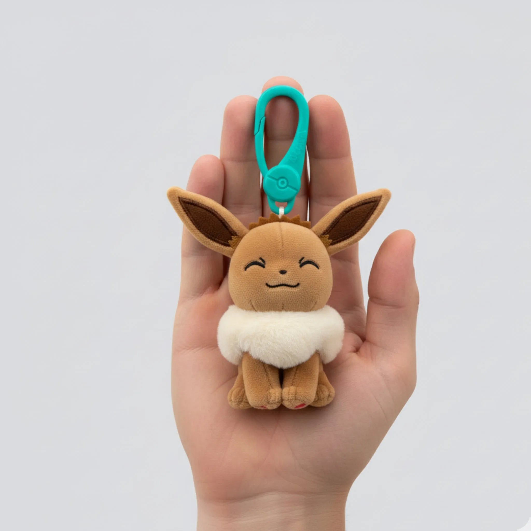 Plush keychain of a cartoon character held in a hand against a white background