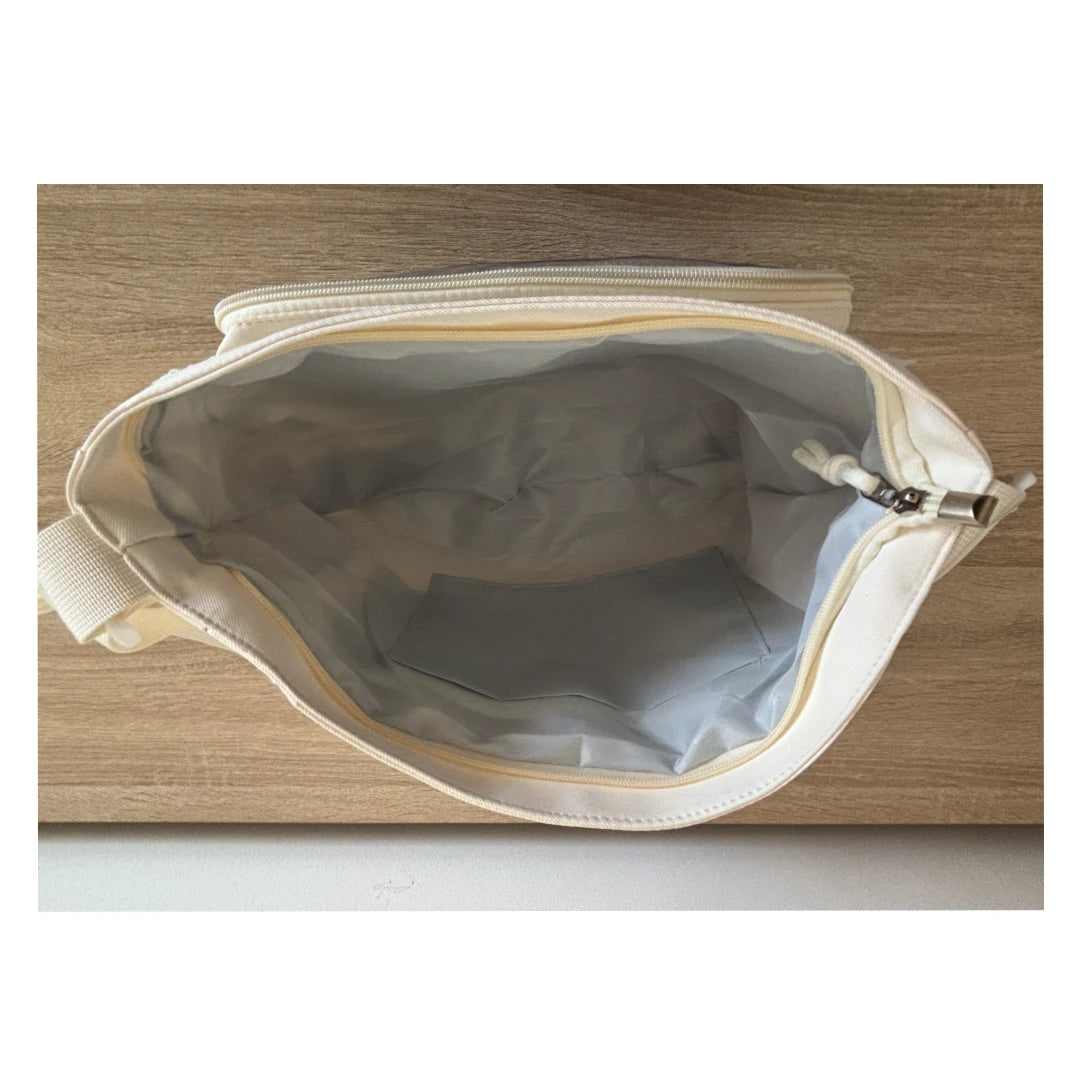 An open cream-colored canvas zippered pouch or organizer, showing a light gray interior lining, photographed from above on a light wood surface.