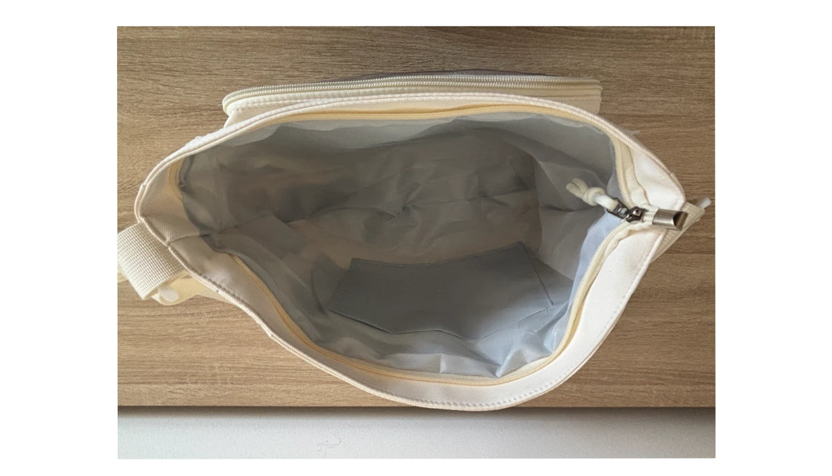 An open cream-colored zippered pouch or small bag, showing a light gray interior lining, photographed from above on a light wood surface.