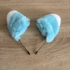 Light blue and white faux fur cat ears headband on a light wood background.