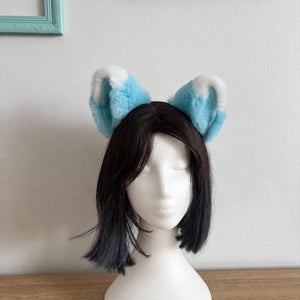 A black bob wig displayed on a white mannequin head, featuring fluffy light blue and white cat ears on a headband.