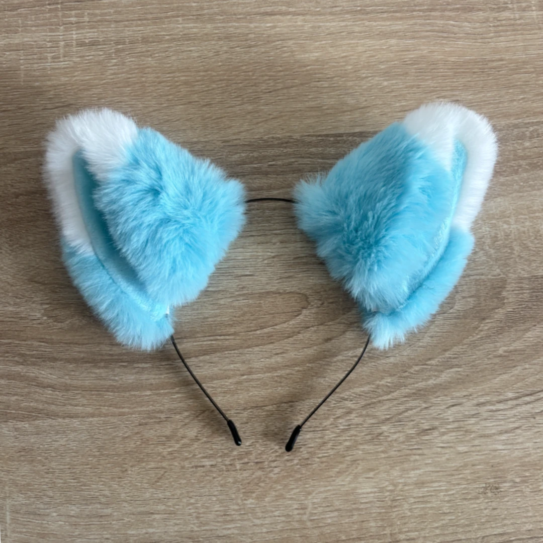 Light blue and white faux fur cat ears headband on a light wood background.