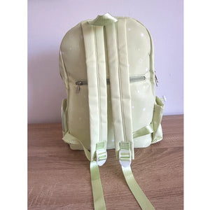 A light green Ita backpack with a subtle white star pattern, shown from the back on a wooden surface against a pale lavender wall.