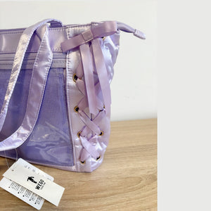 A lavender purple mesh and satin ita handbag with a lace-up front detail, resting on a light wooden surface with its white brand tag visible in the foreground.