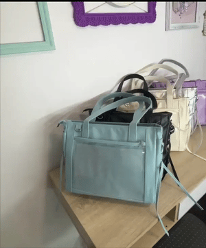 Light blue ita handbag on a wooden surface with other ita bags in the background.