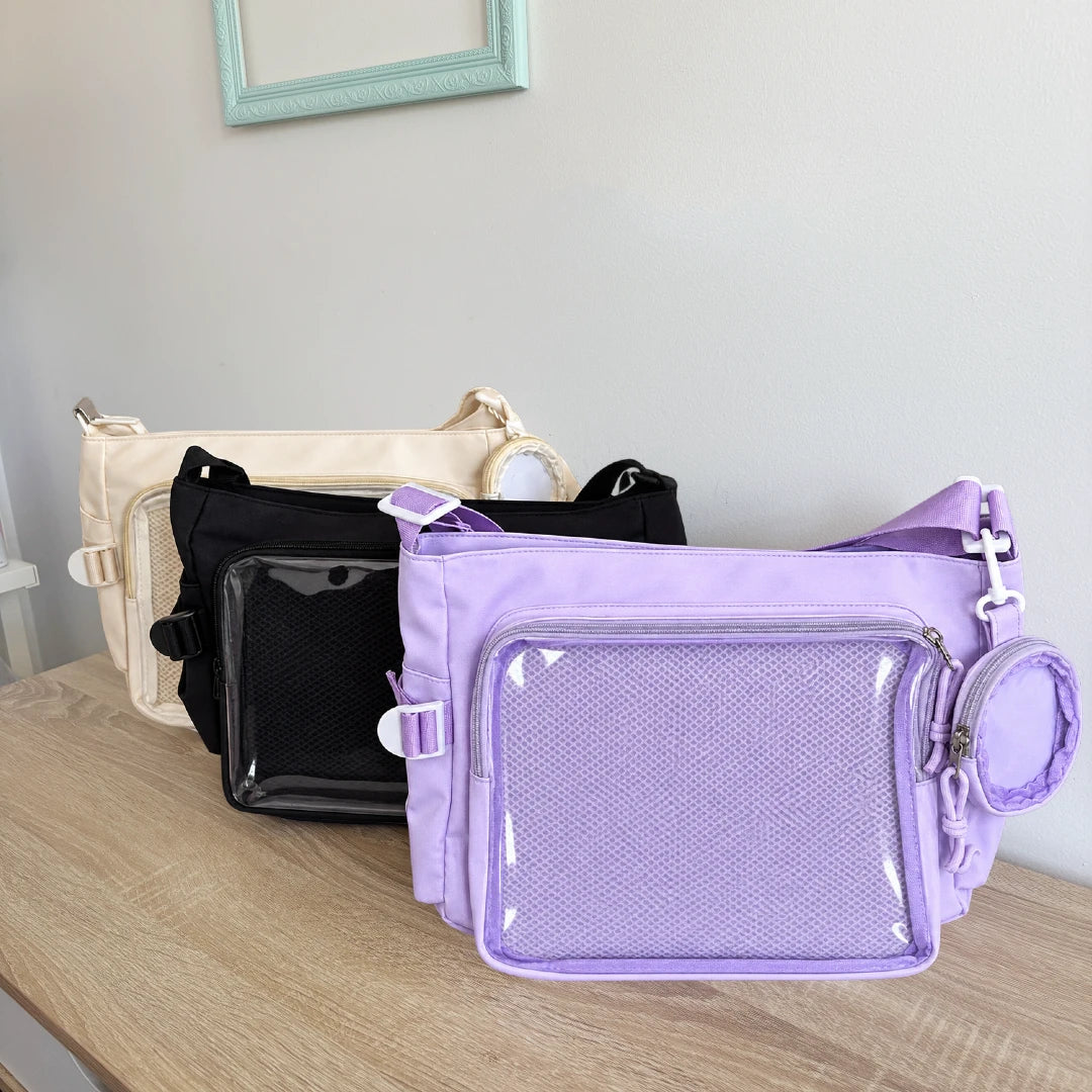 Three crossbody ita bags in cream, black, and lavender purple are displayed on a light wood table against a neutral gray wall.