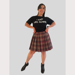 Person wearing a black t-shirt with text and a brown plaid skirt on a plain background