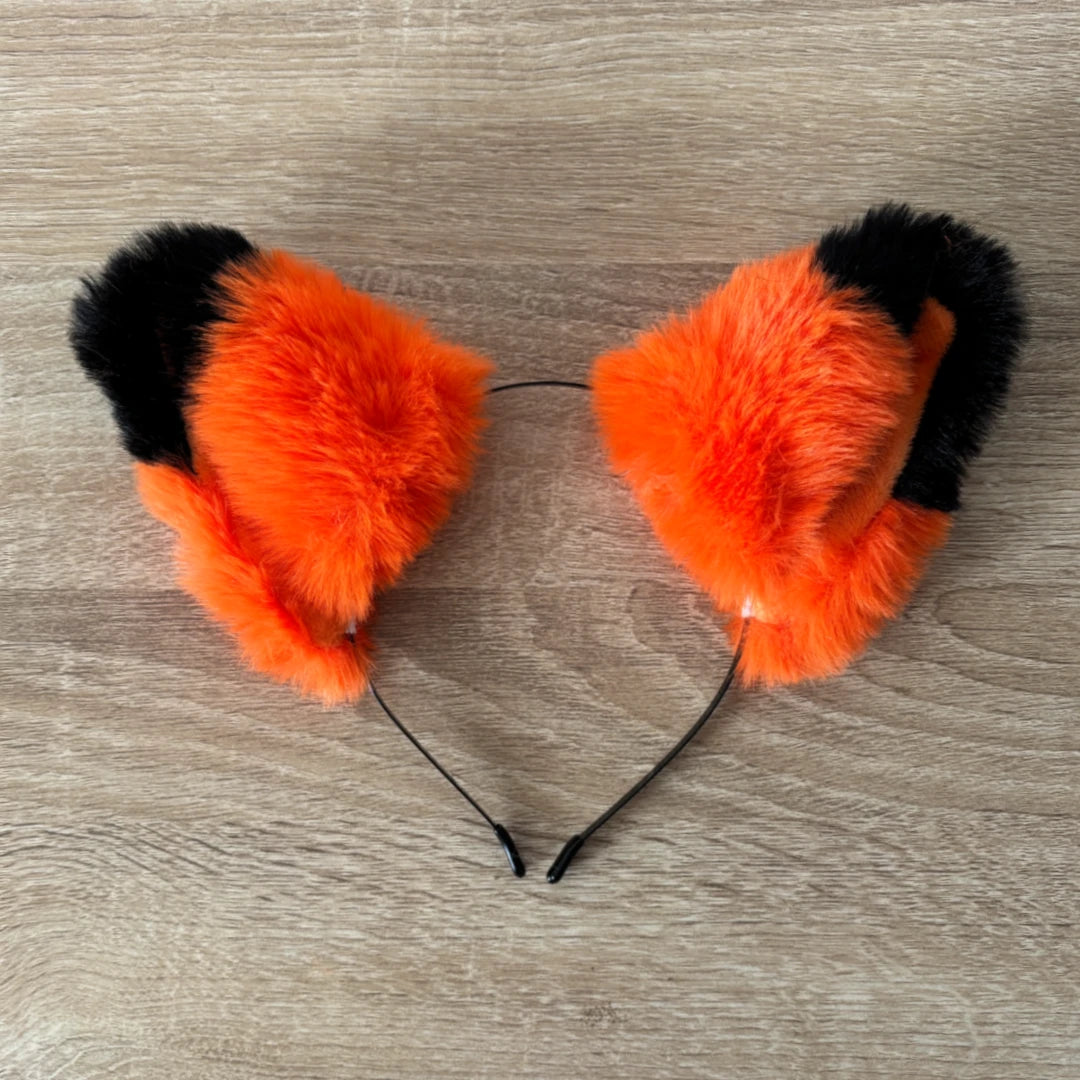 Orange and black faux fur animal cat ears headband displayed on a light wood grain surface.