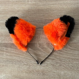 Orange and black faux fur animal cat ears headband displayed on a light wood grain surface.