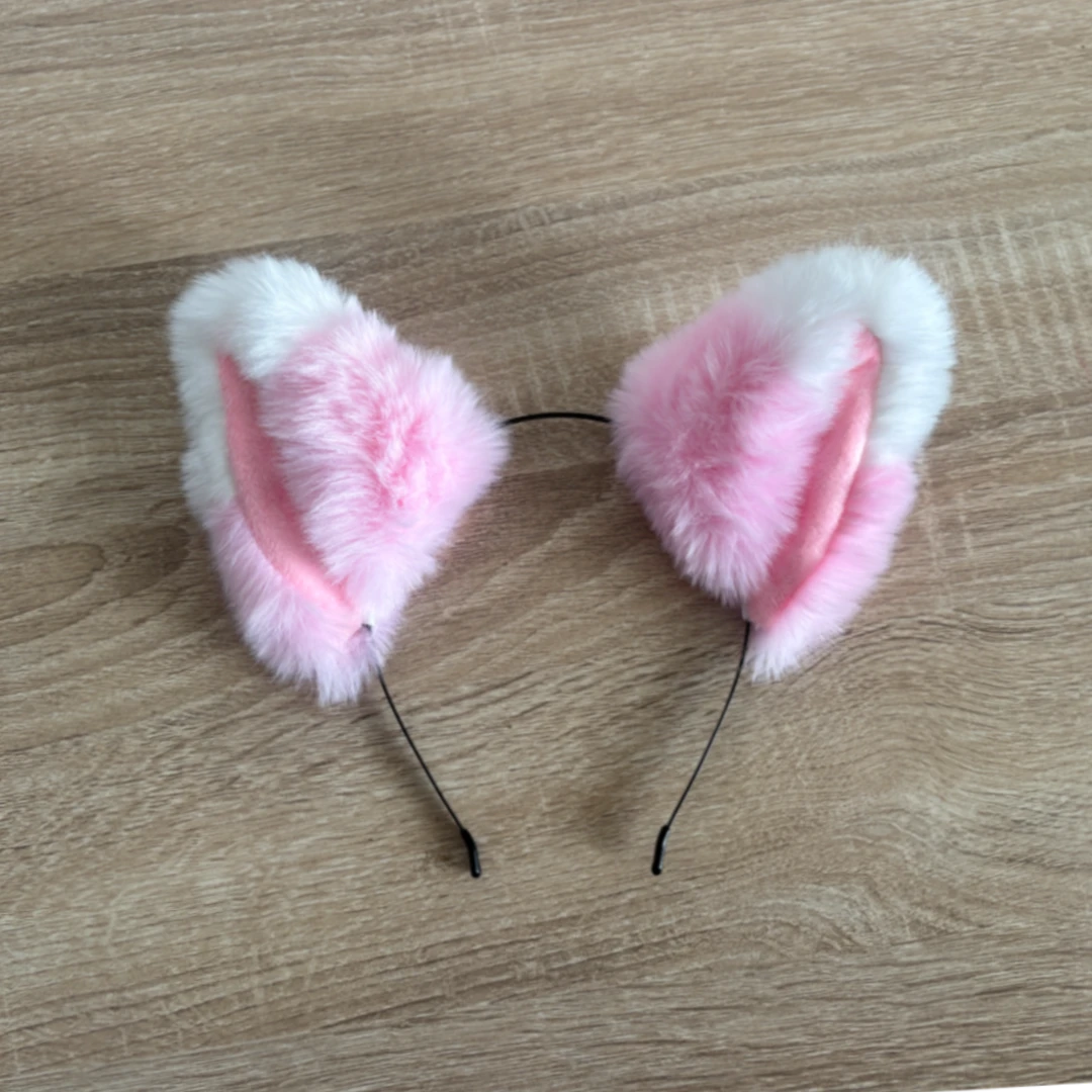 Pink and white faux fur cat ears headband on a light brown wood grain background.