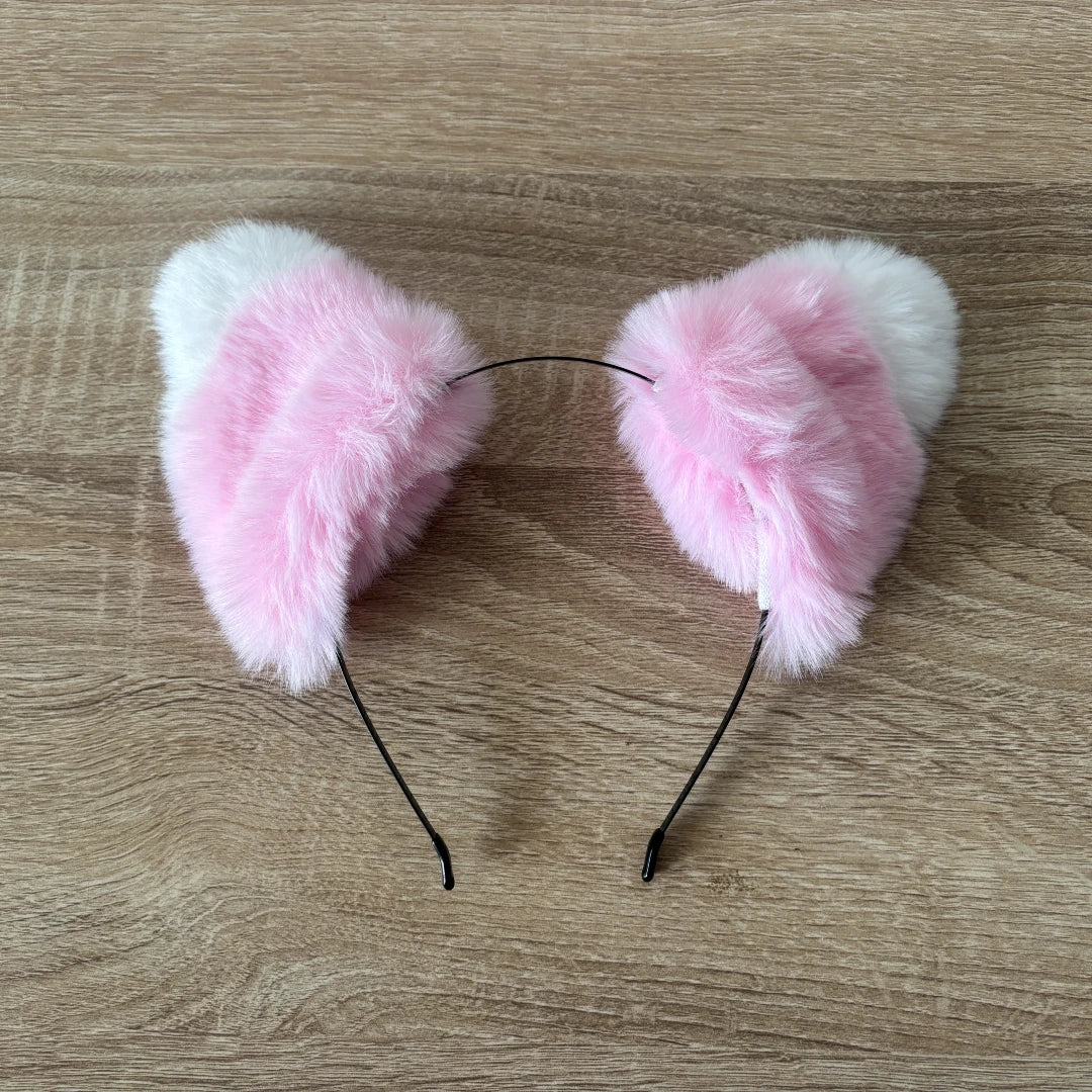 Pink and white faux fur cat ears headband on a light brown wood grain background.