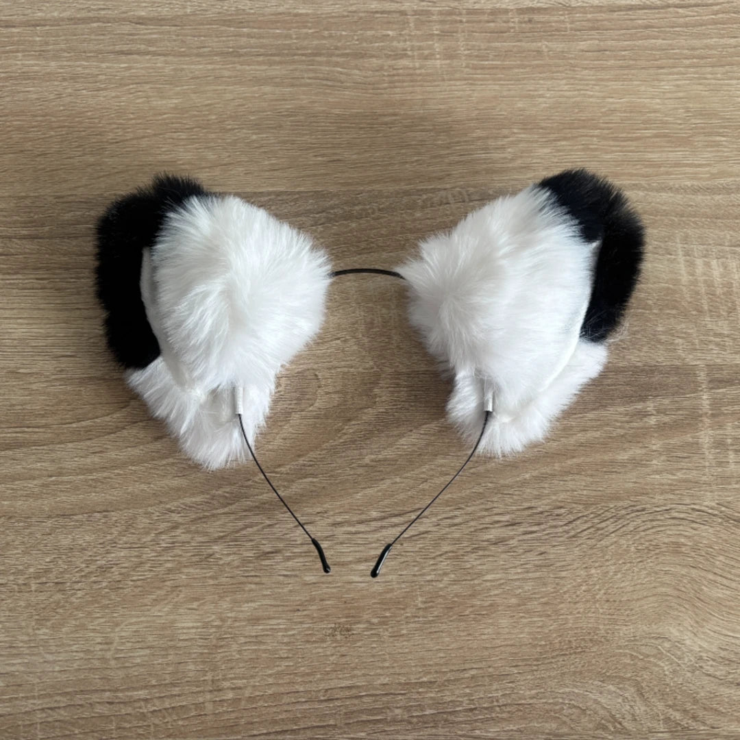 White and black faux fur cat ears headband on a light wood grain background.