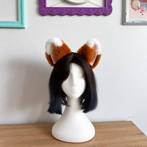 A short black bob wig with fluffy brown and white fox ears on a white mannequin head, displayed on a wooden table against a white wall with framed pictures.