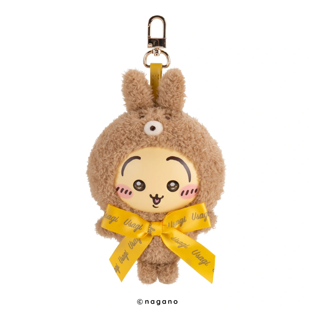 A plush keychain featuring a cute cartoon character in a brown fuzzy bunny suit with a yellow ribbon bow and a gold metal clasp at the top, shown on a plain white background.