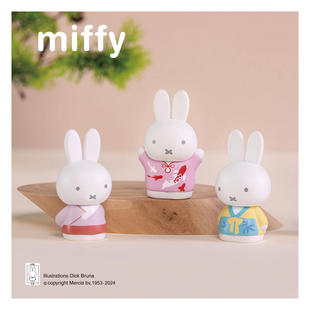 Three miffy figurines in colorful outfits on a wooden stand with a beige background.