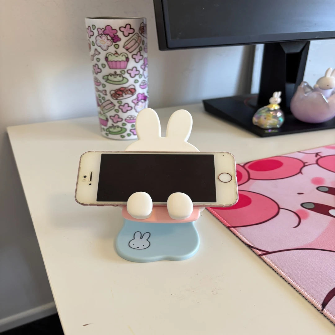 Miffy Phone stand with an iphone on a desk next to a colorful mug and monitor