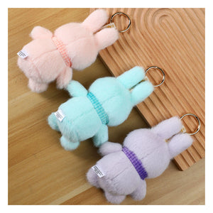 Three plush Miffy official rabbit keychains in pink, green, and gray on a wooden surface.