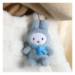 Plush toy Miffy rabbit with a blue scarf hanging on a textured surface