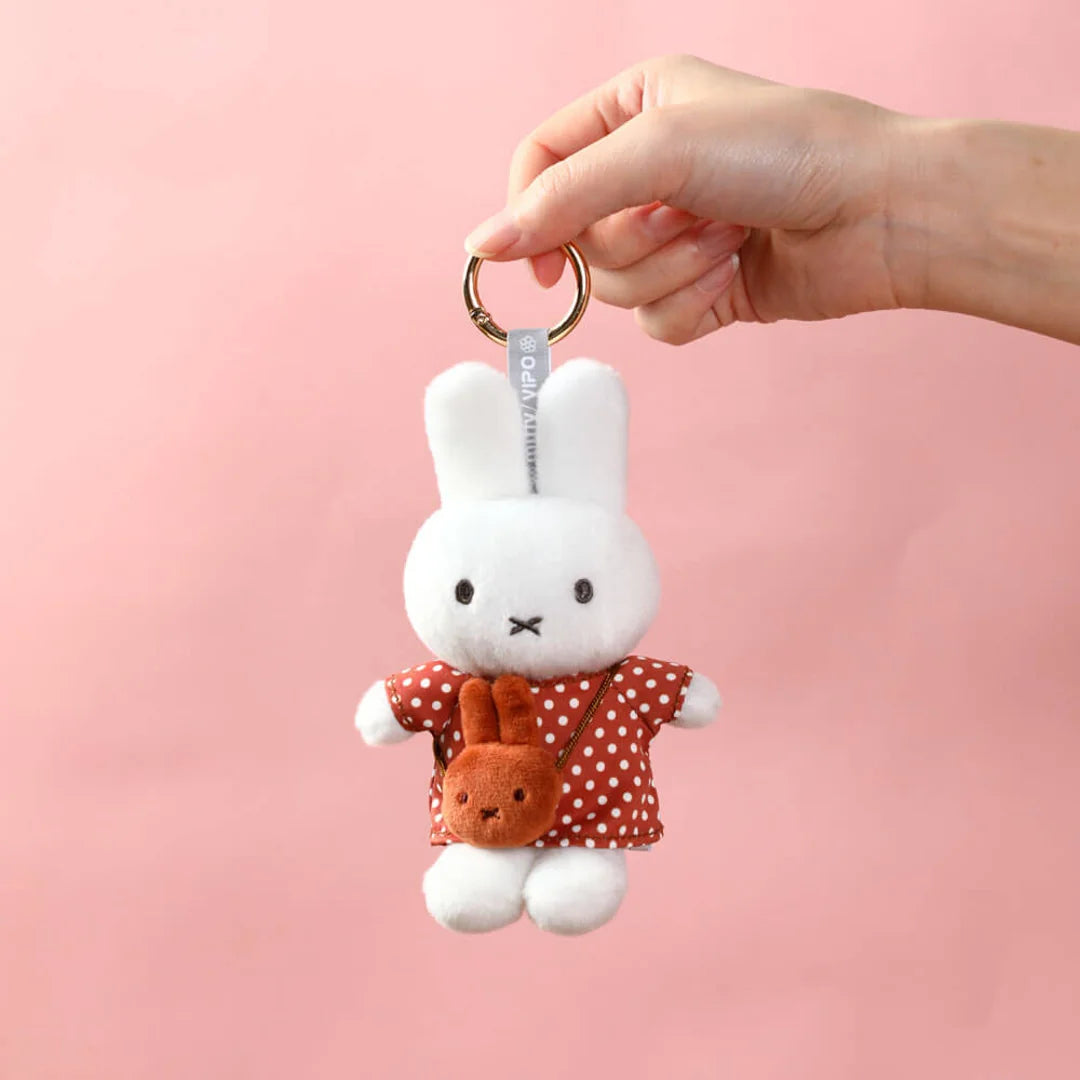 Plush keychain of Miffy white rabbit character with a red polka dot dress on a pink background. Part of Miffy blind box collection