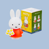 Miffy figurine Miffy with a red dress and flower bouquet next to its packaging 