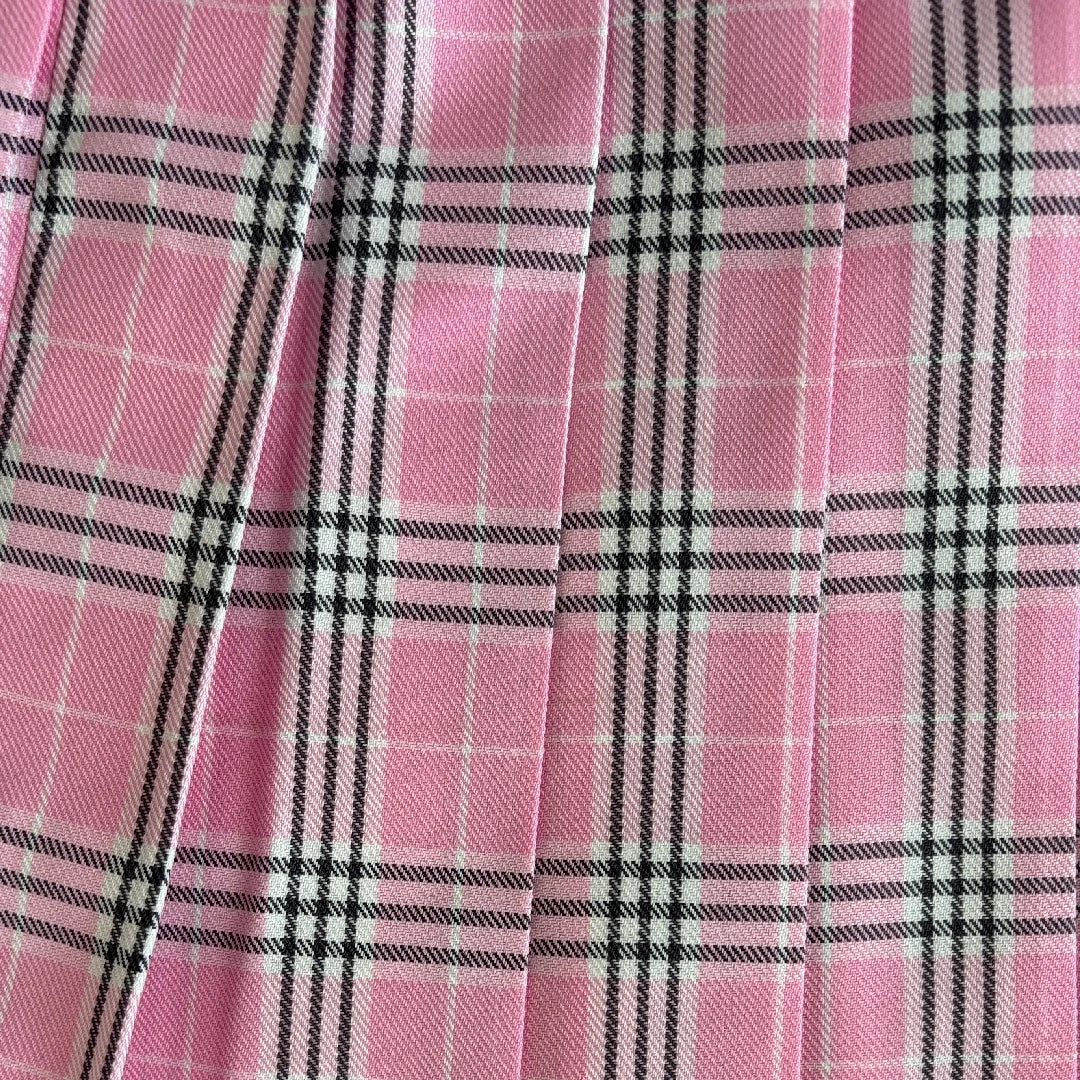 Pink pleated fabric with a black and white plaid pattern, shown in a close-up view highlighting the texture and folds.